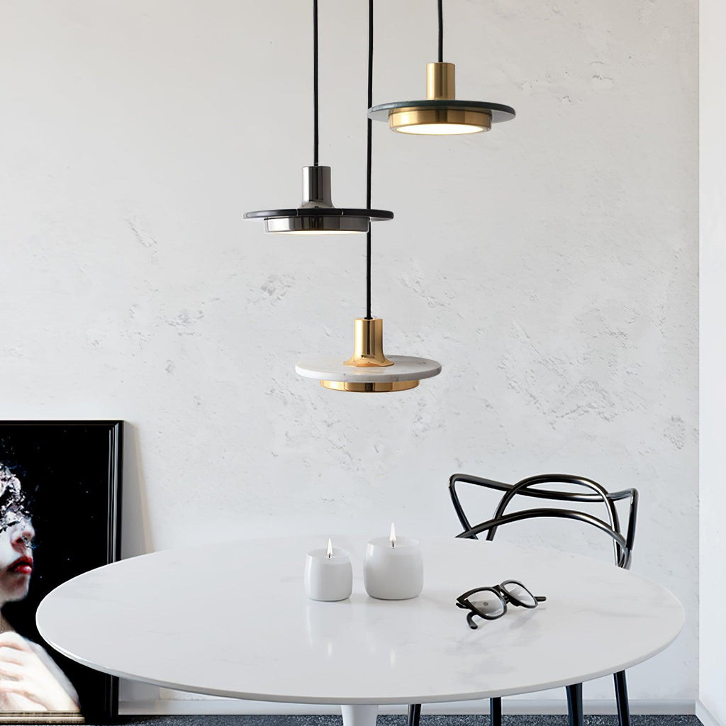 Three Clérachic pendant lights in gold, black and white marble hang low over a round table set with candles.