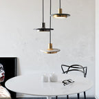 Three Clérachic pendant lights in gold, black and white marble hang low over a round table set with candles.