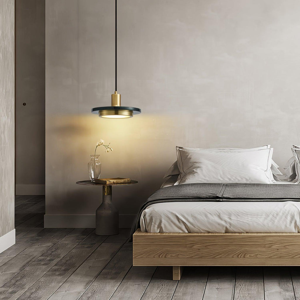 A gold-and-white-marble Clérachic pendant light glows beside a wooden bed, lighting a small vase on the side table.