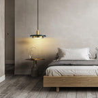 A gold-and-white-marble Clérachic pendant light glows beside a wooden bed, lighting a small vase on the side table.