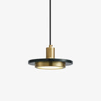 Close-up of a Clérachic pendant's dark stone disc glowing warm along its inner ring, its slim brass fitting bare against white.