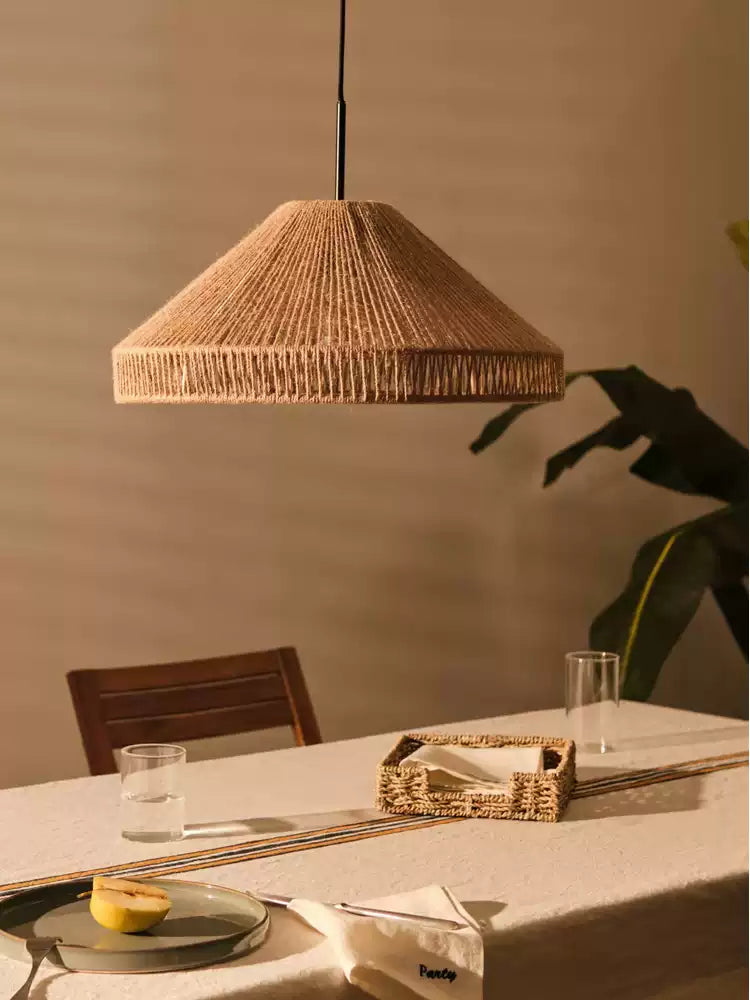 Beside a wood chair, this Clérachic pendant lights a linen-covered table set with glassware and a woven tray.