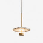 Photographed in brushed brass against white, this Clérachic pendant suspends its round alabaster disc from a slender stem.