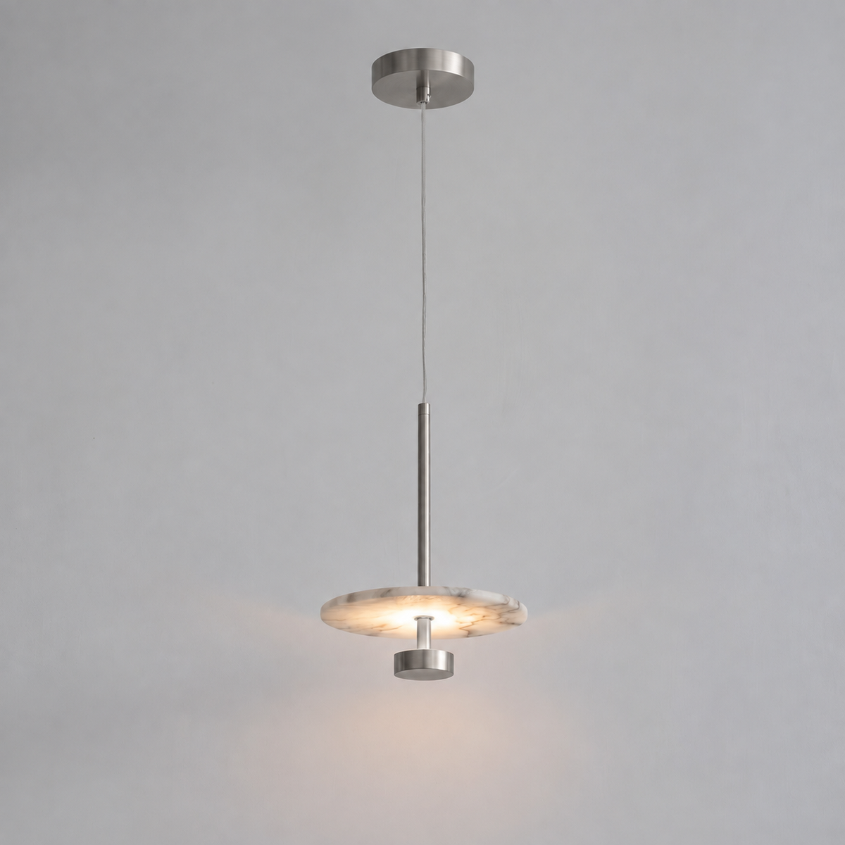 In brushed nickel, this Clérachic pendant hangs its flat alabaster disc from a slim rod against grey.