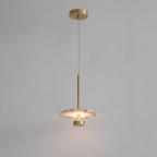 Seen lit in full against grey, this brass Clérachic pendant hangs its glowing disc from a tall brass stem.