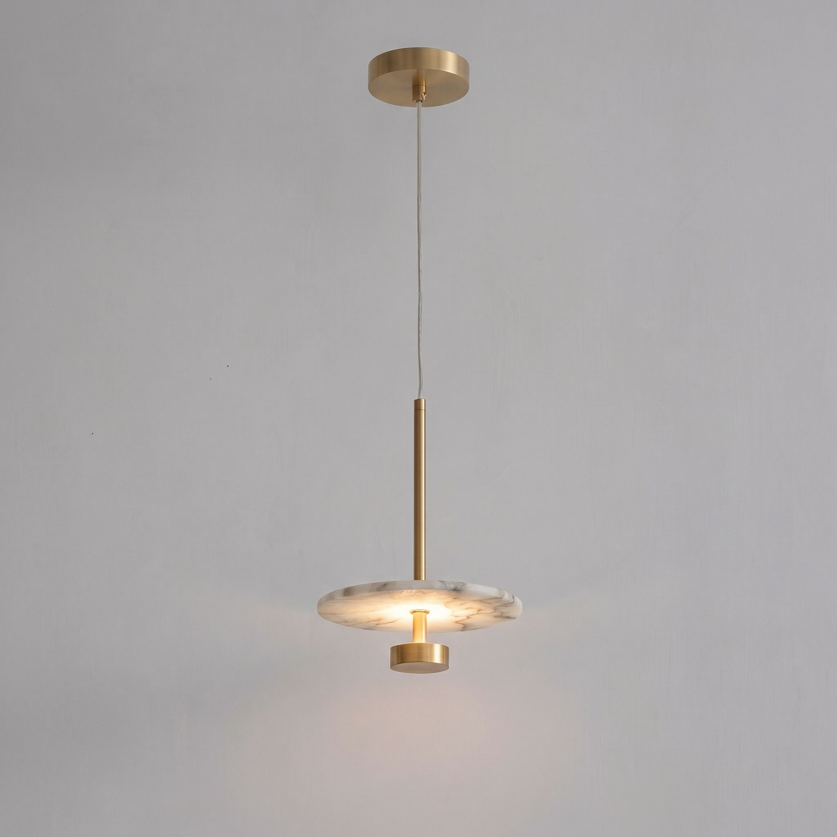 Seen lit in full against grey, this brass Clérachic pendant hangs its glowing disc from a tall brass stem.