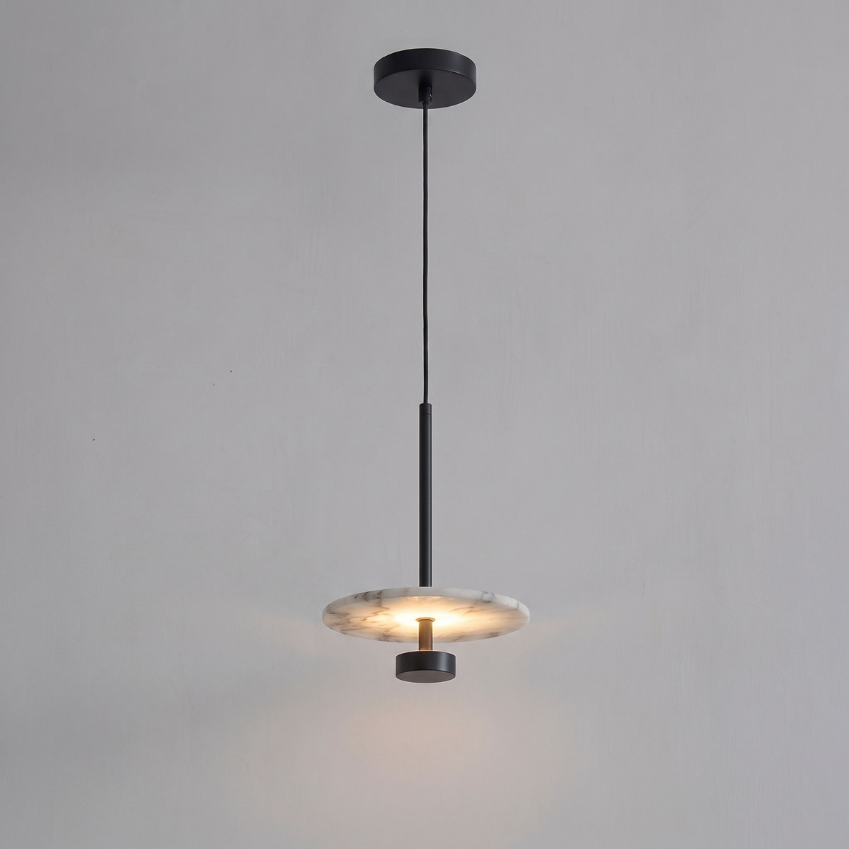 Shown lit against grey, this black Clérachic pendant drops its glowing alabaster disc from a slender rod.
