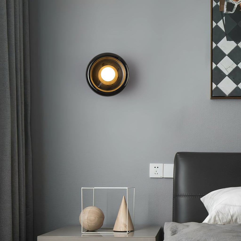 Wider view of the same Clérachic black marble wall sconce lit in the bedroom, showing more of the grey wall and headboard.