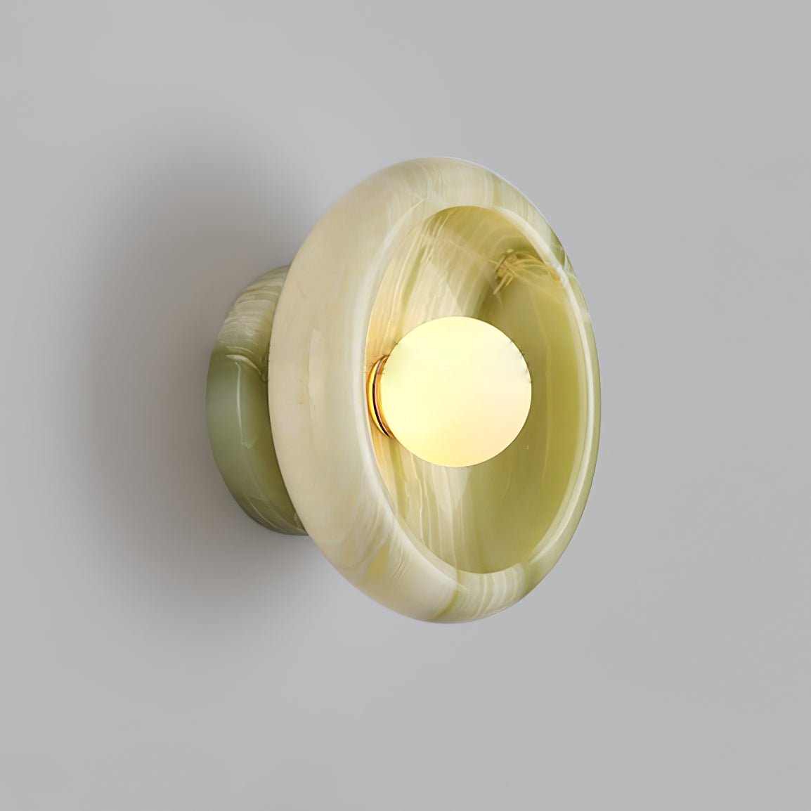 Clérachic wall sconce in swirled green jade, its marbled pattern lit from the glowing bulb at centre.