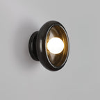Clérachic wall sconce in glossy black marble with an amber-tinted glass shade, lit against a grey wall.