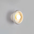 Close-up of a Clérachic white marble wall sconce lit against a grey wall, its veined interior visible around the bulb.