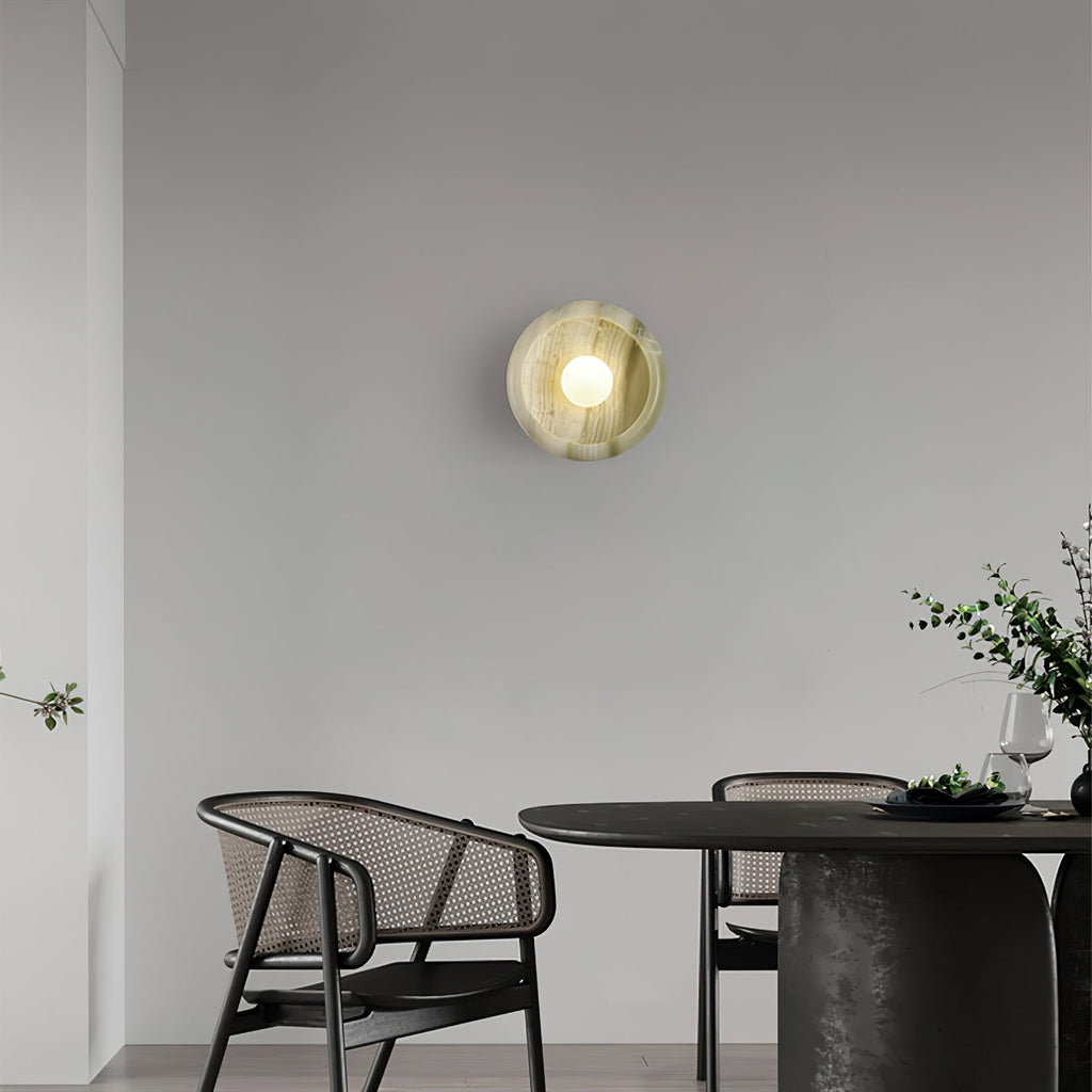 Clérachic jade wall sconce lit above a dining area furnished with black woven chairs and a round table.