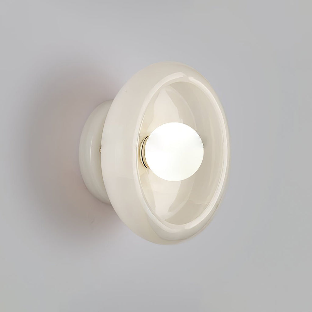 Clérachic wall sconce with a glossy white stone disc lit close up against a plain grey wall.
