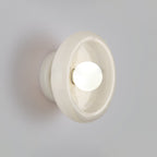 Clérachic wall sconce with a glossy white stone disc lit close up against a plain grey wall.