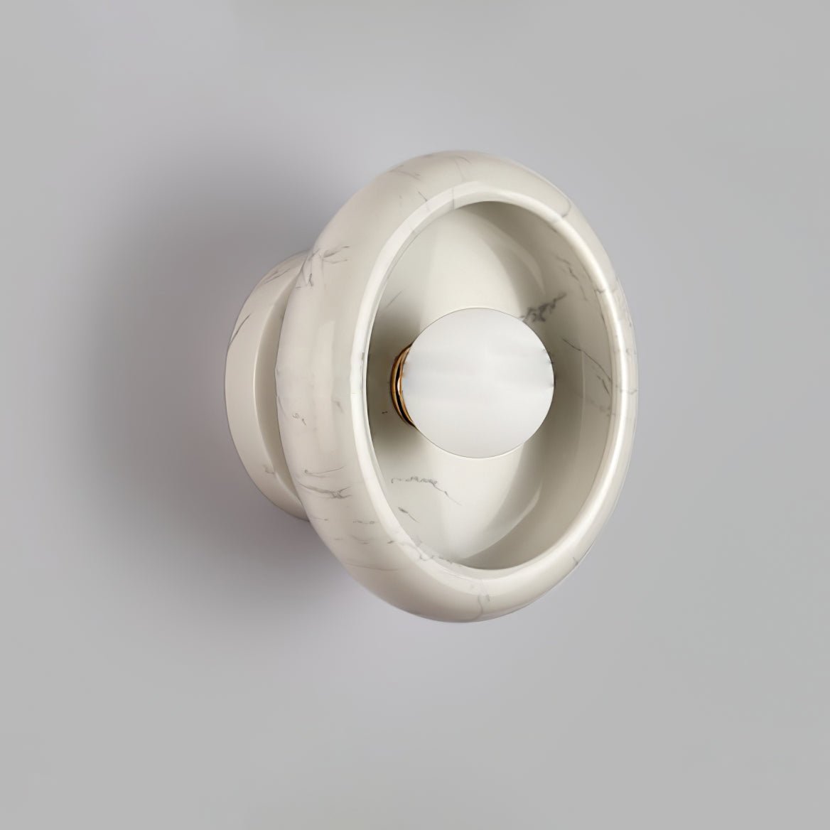 Clérachic wall sconce in veined white marble, its grey striations visible around the glowing central bulb.