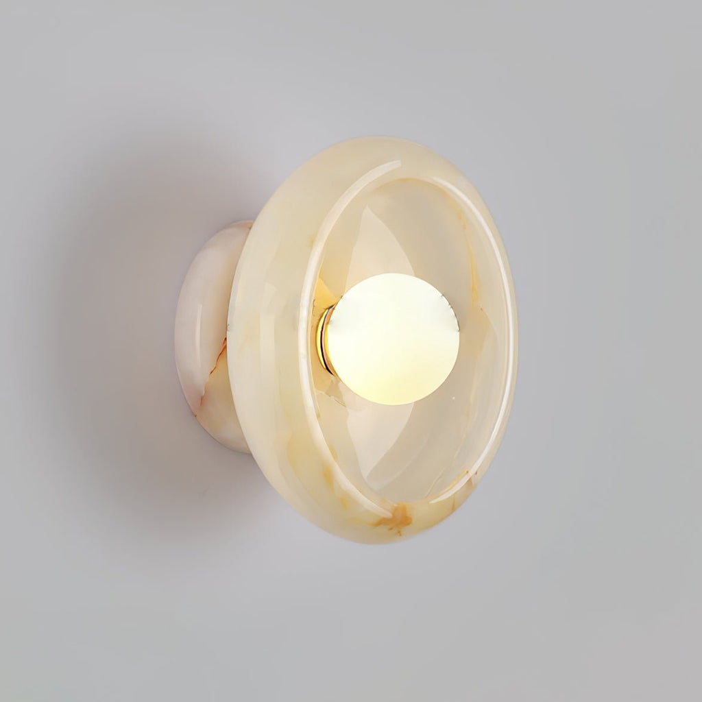 Clérachic wall sconce in warm beige jade with soft amber marbling, lit against a plain grey wall.