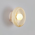 Clérachic wall sconce in warm beige jade with soft amber marbling, lit against a plain grey wall.