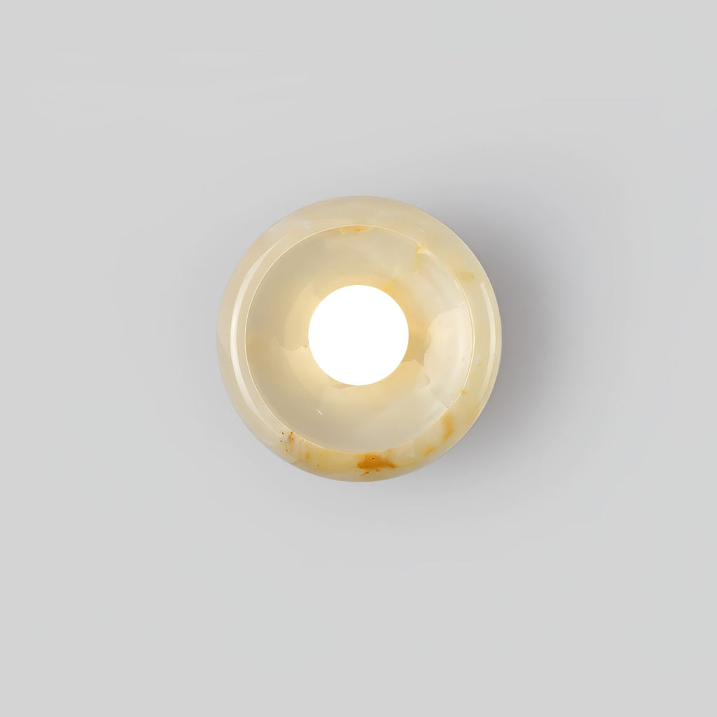 Clérachic beige jade wall sconce lit on a plain white background, showing the disc's warm veined surface.