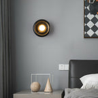Clérachic black marble wall sconce lit above a bedroom nightstand with a ball-and-cone ornament, beside a dark headboard.