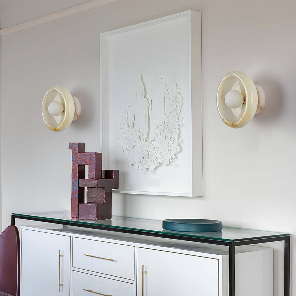 Two Clérachic jade wall sconces flank a framed mirror above a white console table holding small sculptures.