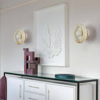 Two Clérachic jade wall sconces flank a framed mirror above a white console table holding small sculptures.