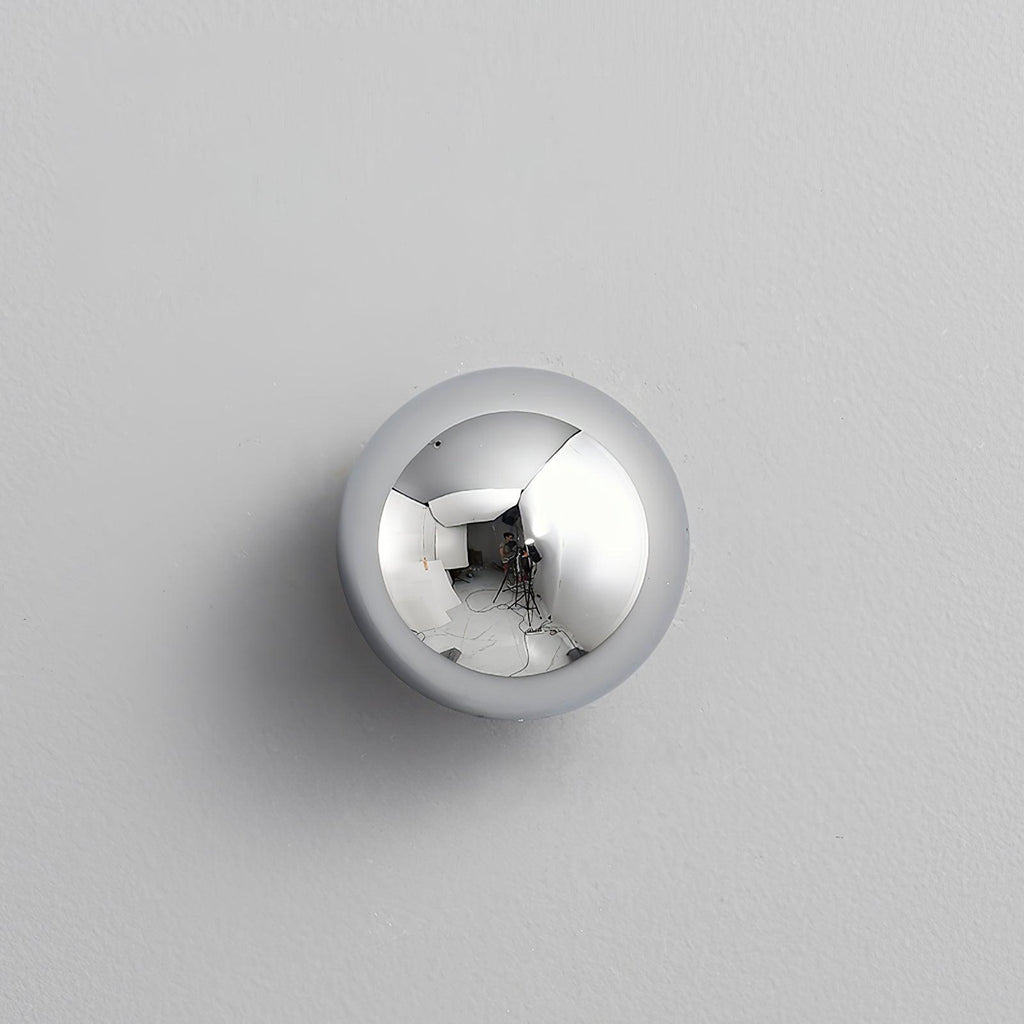 Polished sphere wall sconce lit against a dark wall