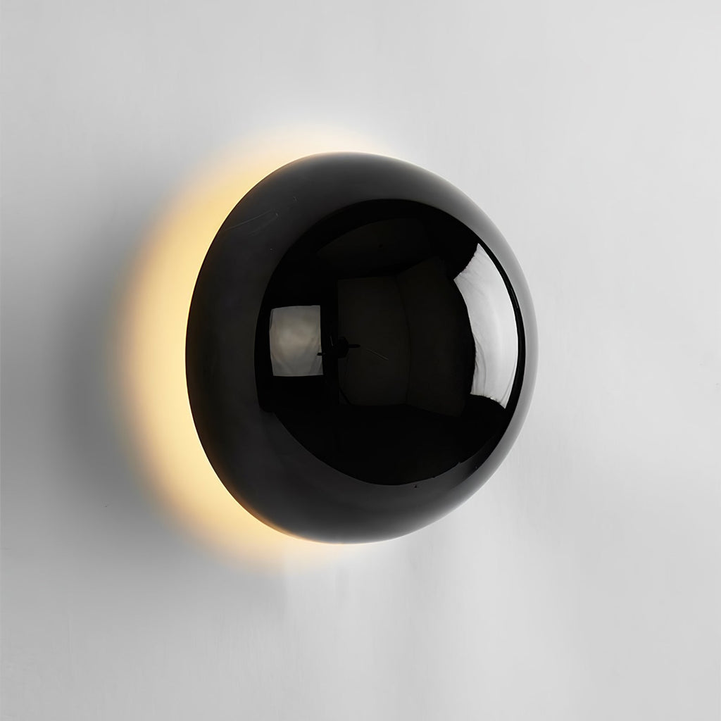 Polished sphere wall sconce glowing softly on a wall