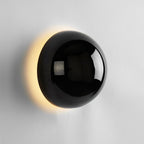 Polished sphere wall sconce glowing softly on a wall