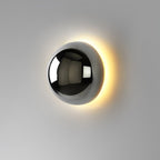Polished sphere wall sconce lit warmly against a wall