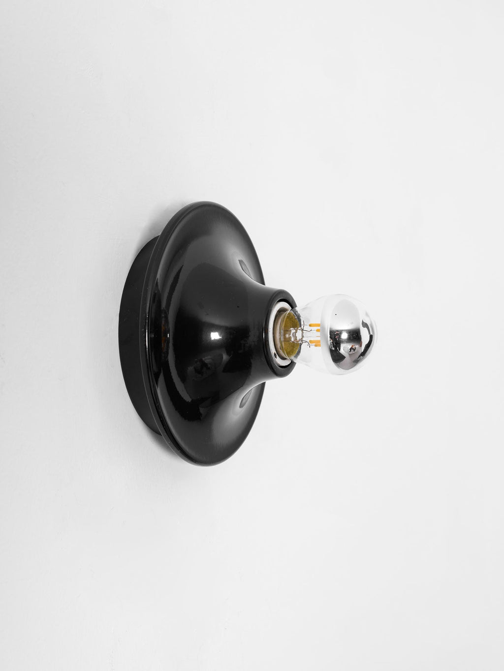 Eclipta wall sconce reflecting warm light from its mirrored bulb