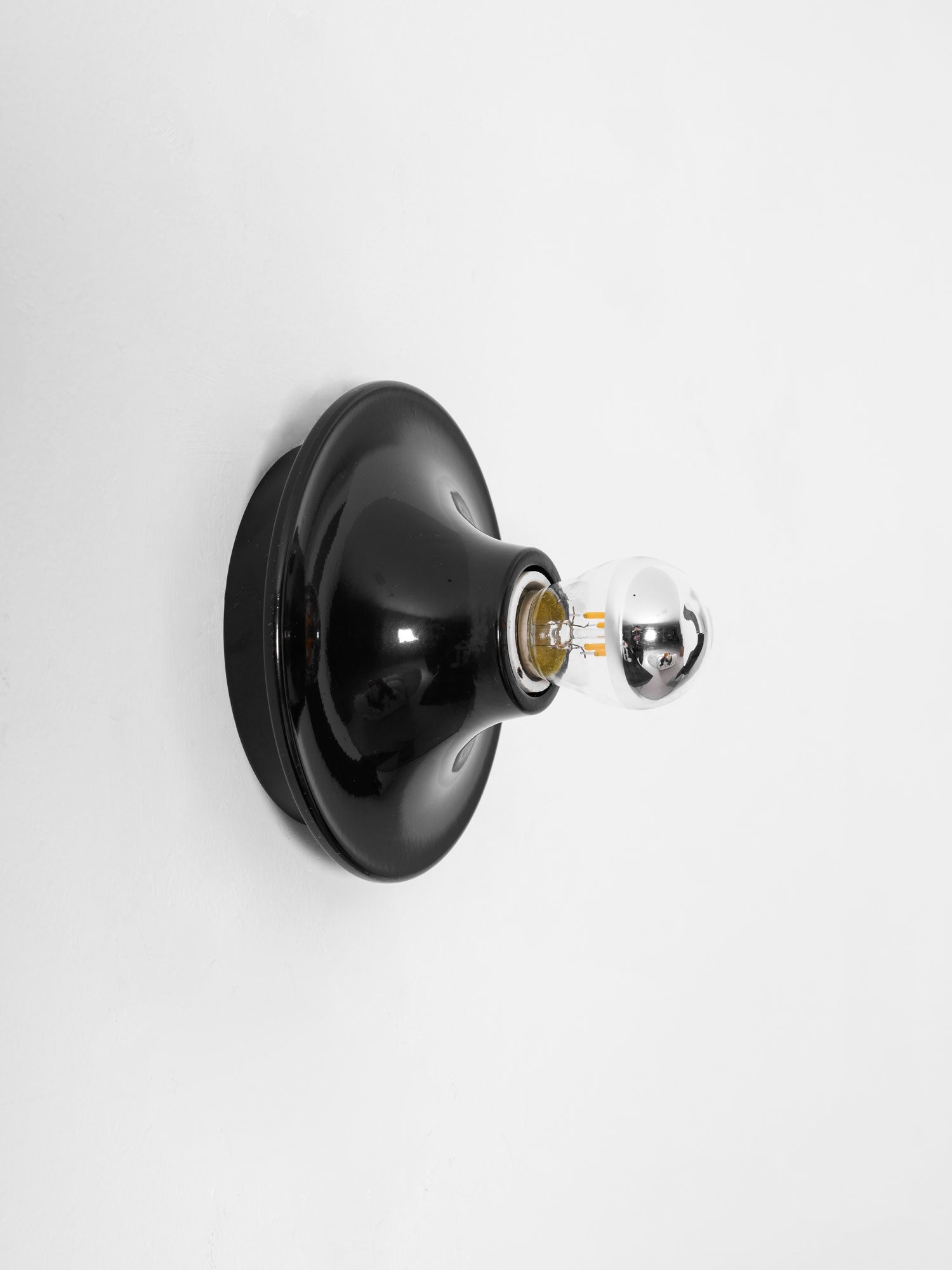 Eclipta wall sconce reflecting warm light from its mirrored bulb