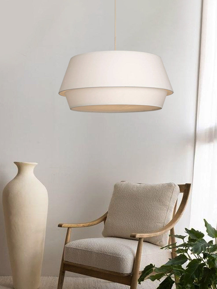 In a room corner, this Clérachic pendant hangs near a tall cream vase and a bouclé armchair with a cushion.