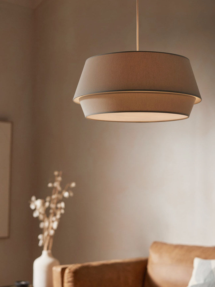 A taupe-toned version of this Clérachic pendant hangs above a rust-orange sofa with a vase of dried stems.