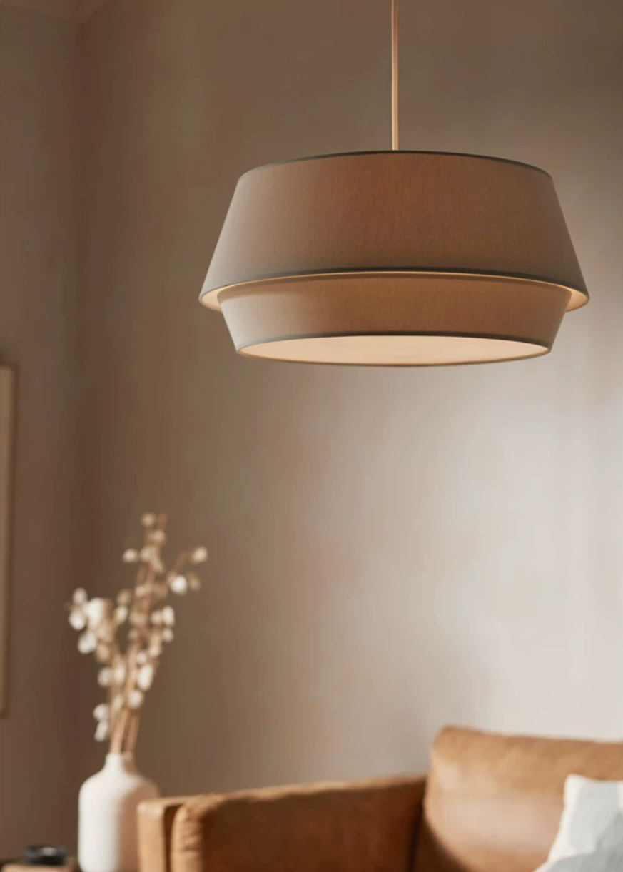 A closer view of this Clérachic pendant in taupe, lit warmly above the rust-orange sofa.