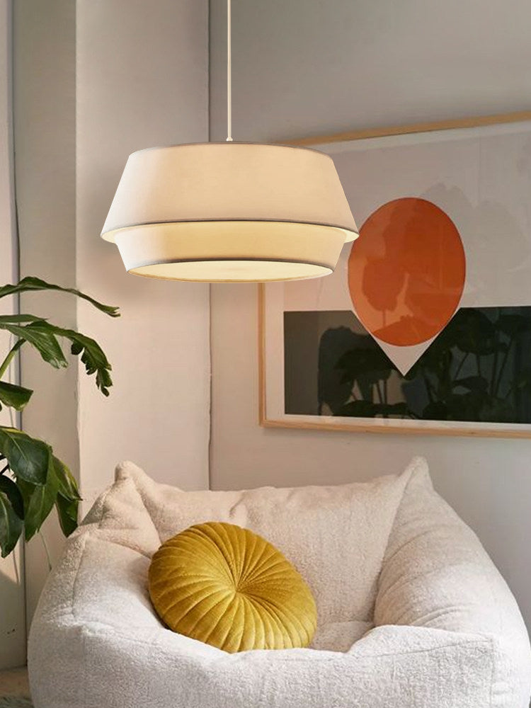Lit warmly, this Clérachic pendant glows above a bouclé armchair with a mustard round cushion and a leafy plant.