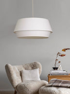 On a plain grey backdrop, this Clérachic pendant hangs above a cream bouclé armchair with patterned cushions.
