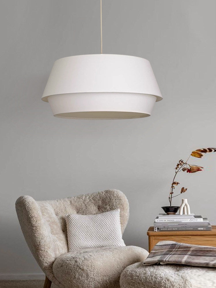 On a plain grey backdrop, this Clérachic pendant hangs above a cream bouclé armchair with patterned cushions.