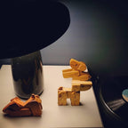 Black marble Clérachic table lamp on a dark table beside carved wooden dog figures, in a dimly lit moody room setting.