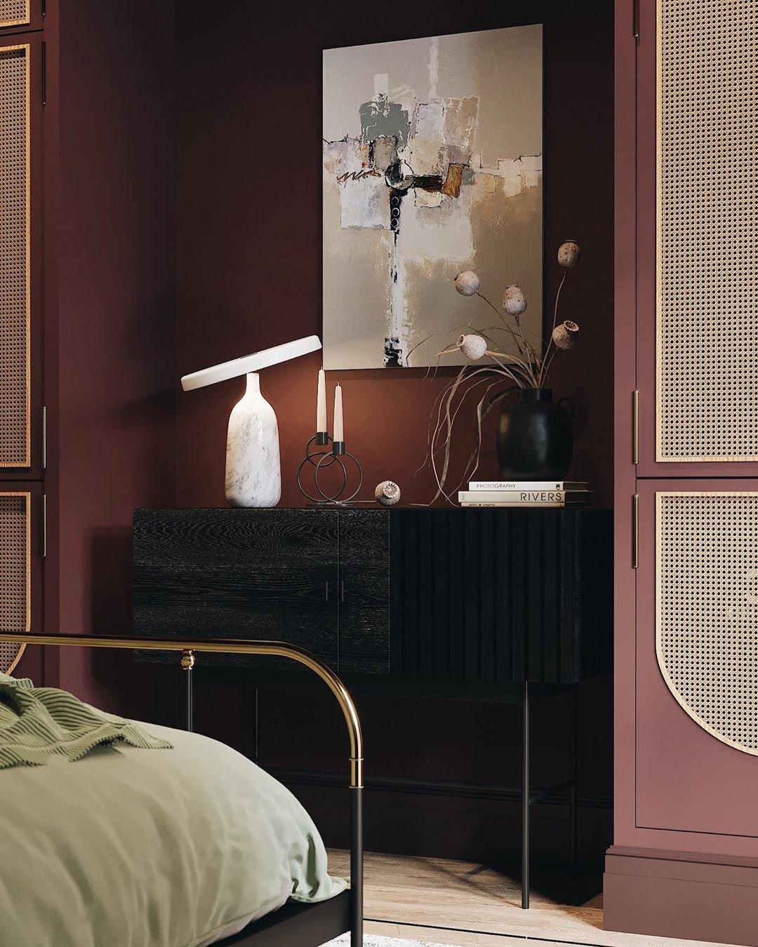 White marble Clérachic table lamp on a dark sideboard in a wine-coloured bedroom, beside lit candles and framed art.