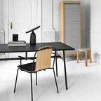 Black Clérachic table lamp on a black desk in a bright white study, beside a wood-slat room divider and a small stool.