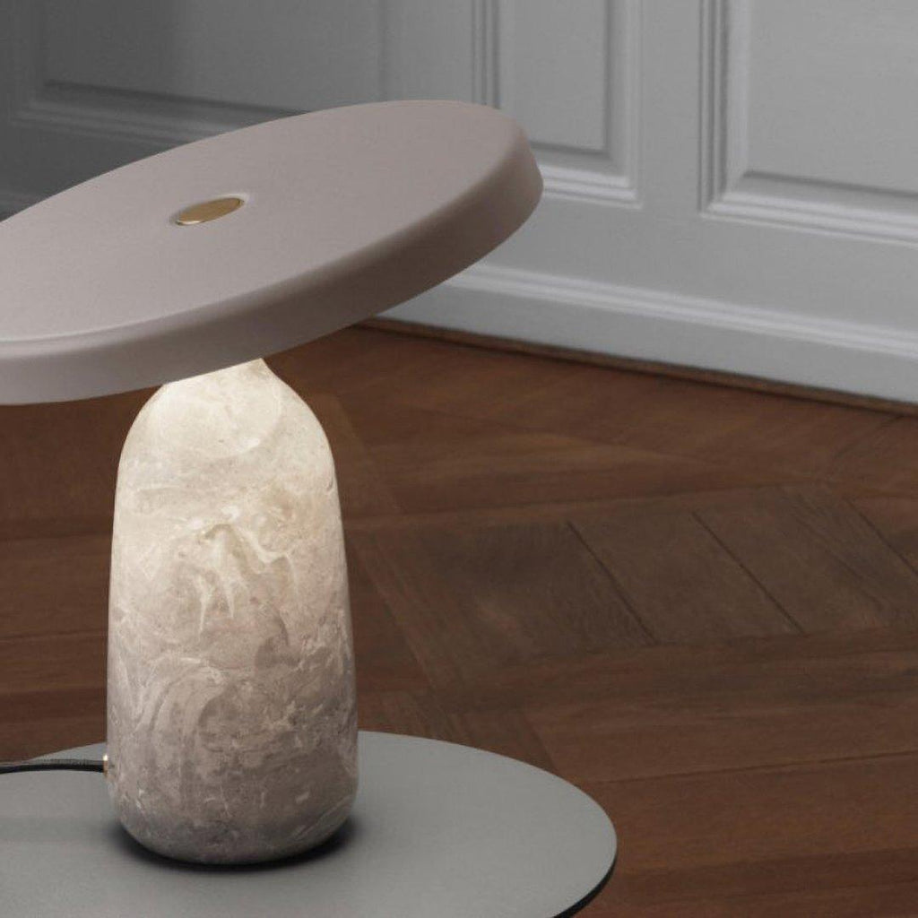 Clérachic table lamp on a round plinth in a wood-panelled room, its disc shade angled above the base on a parquet floor.