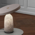Clérachic table lamp on a round plinth in a wood-panelled room, its disc shade angled above the base on a parquet floor.