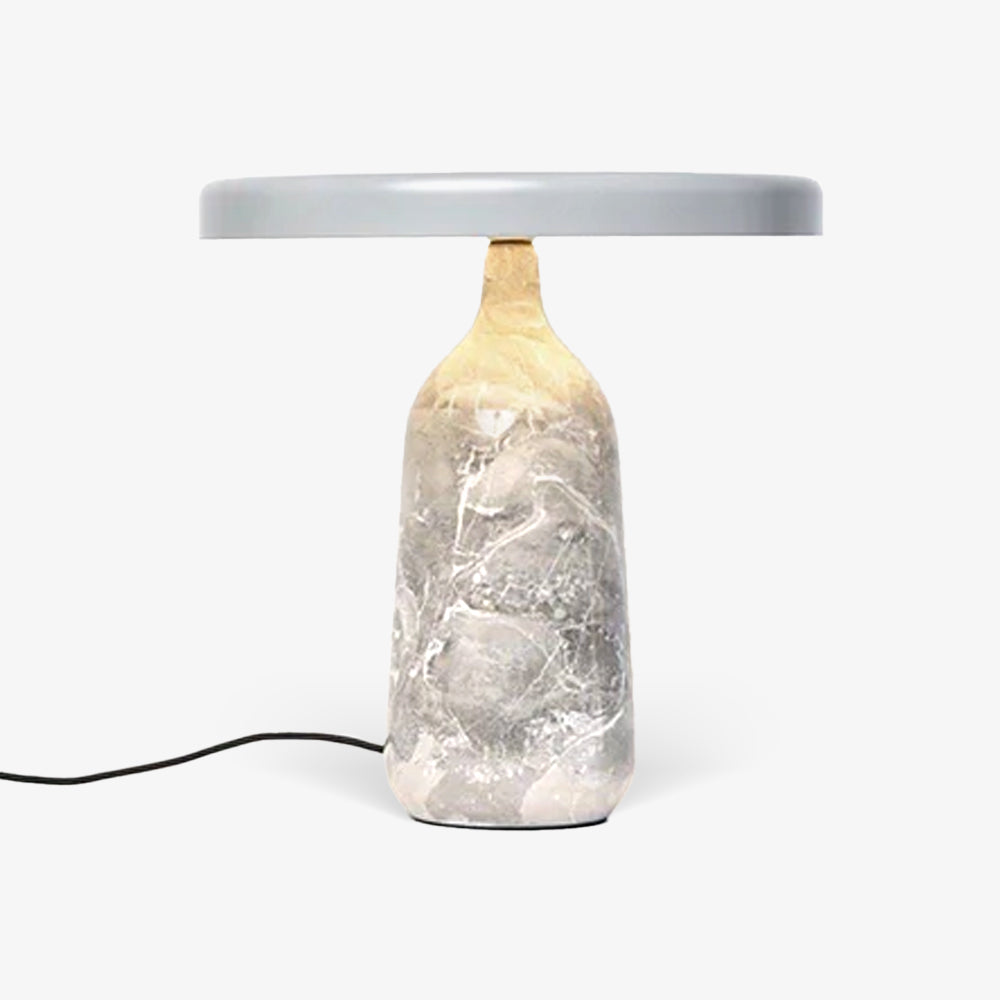 Grey marble Clérachic table lamp lit warm against a plain background, its disc shade held level above the softly glowing base.
