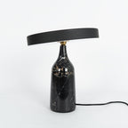 Black marble Clérachic table lamp with visible gold veining, disc shade held level, shown on a plain white background.