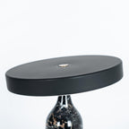 Black marble Clérachic table lamp with its disc shade angled at a steep tilt, cropped close on a white background.