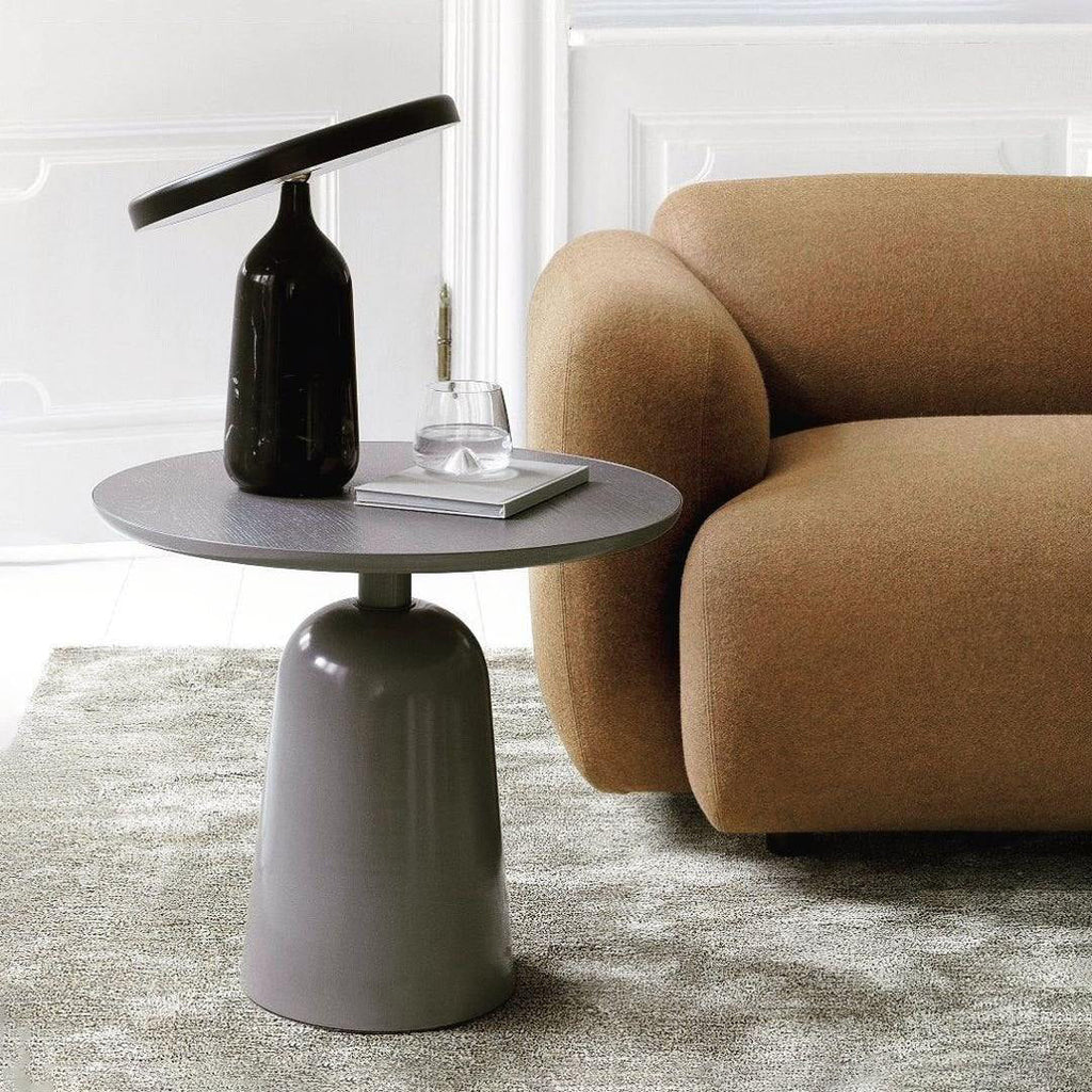 A round-top pedestal side table from the Clérachic collection, styled with a dark vase and glass beside a tan sofa.