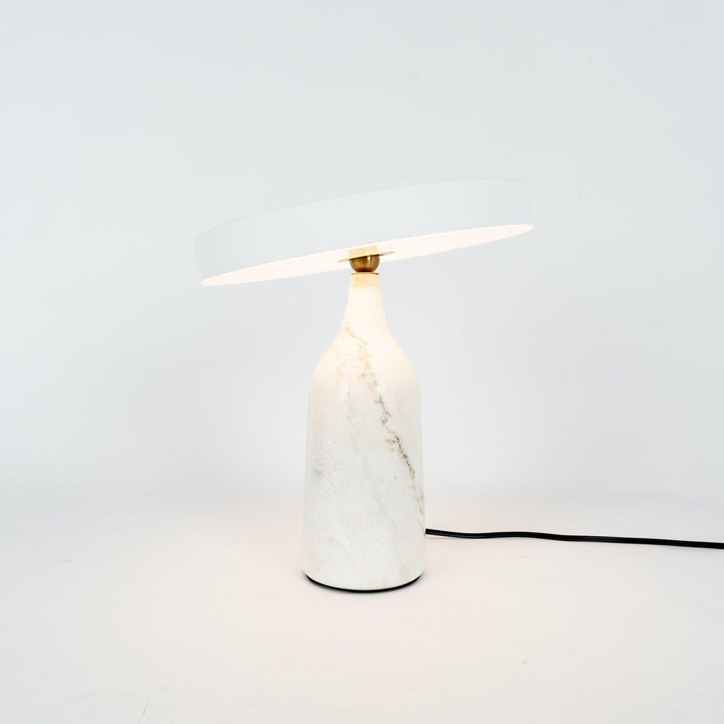 White marble Clérachic table lamp with its disc shade tilted at a steep angle, shown with its cord on white.