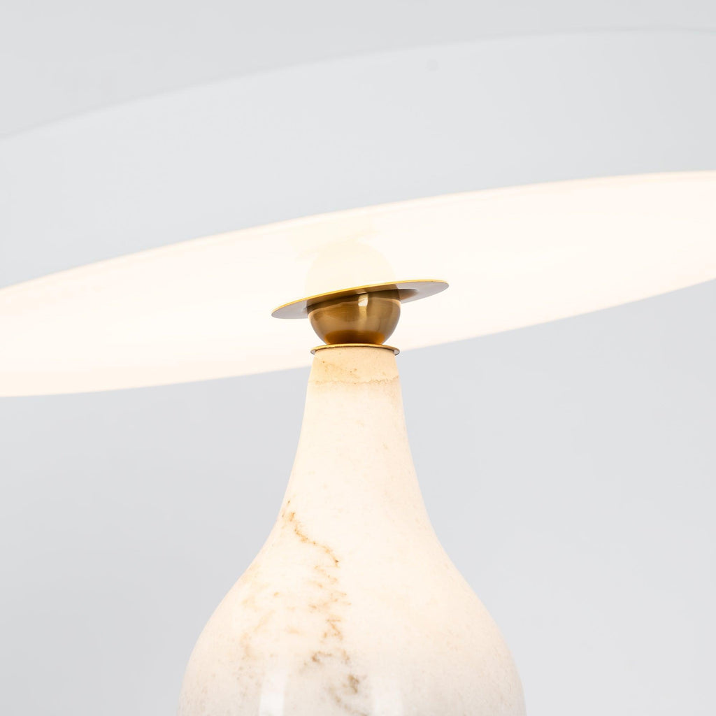 Close-up of the lit Clérachic table lamp's white marble neck and brass joint, glowing beneath the tilted shade.