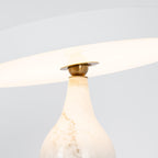 Close-up of the lit Clérachic table lamp's white marble neck and brass joint, glowing beneath the tilted shade.