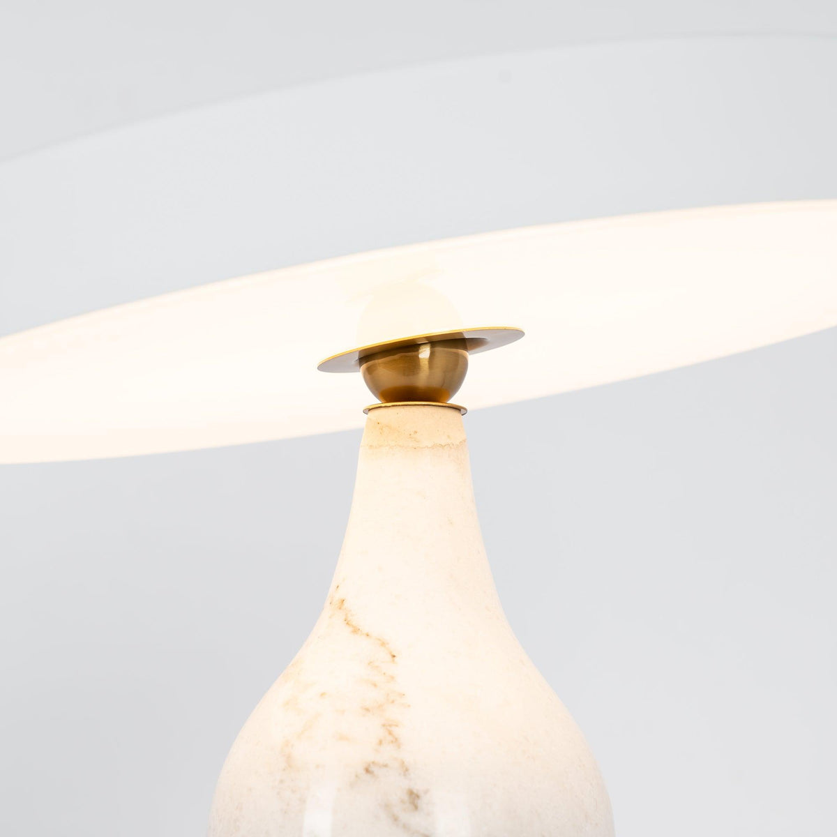 Close-up of the lit Clérachic table lamp's white marble neck and brass joint, glowing beneath the tilted shade.